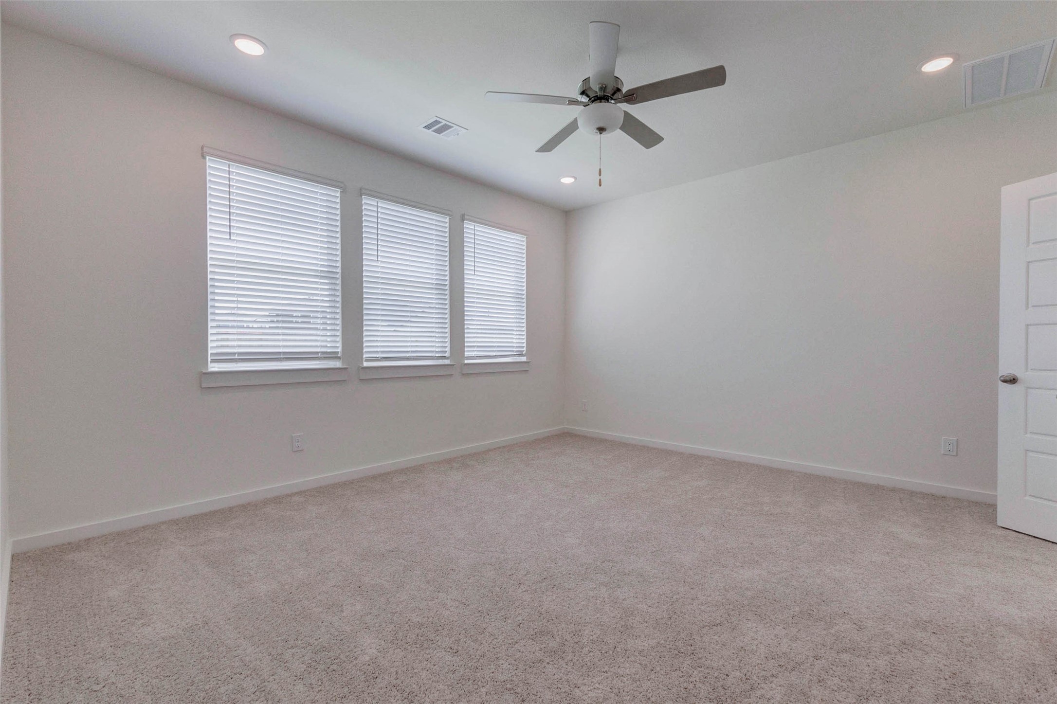 1206 Hemet Court Rosharon, TX 77583 - Photo 10 of 21 Spacious primary bedroom with soft neutral carpet, three large windows, recessed lighting, and a ceiling fan for added comfort. The clean white walls and natural light create a bright, move-in-ready retreat with plenty of flexibility designed to suit a variety of furniture layouts.