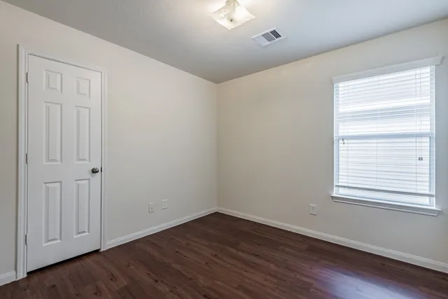 a view of an empty room with wooden floor and a window