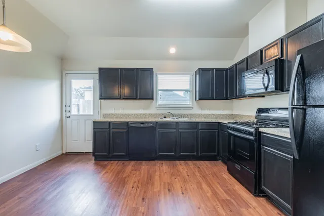 a kitchen with stainless steel appliances granite countertop a refrigerator a sink dishwasher a stove and wooden cabinets with wooden floor