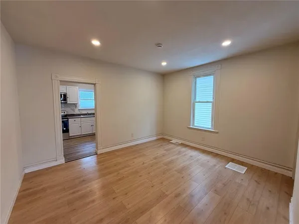 a view of empty room with wooden floor and kitchen
