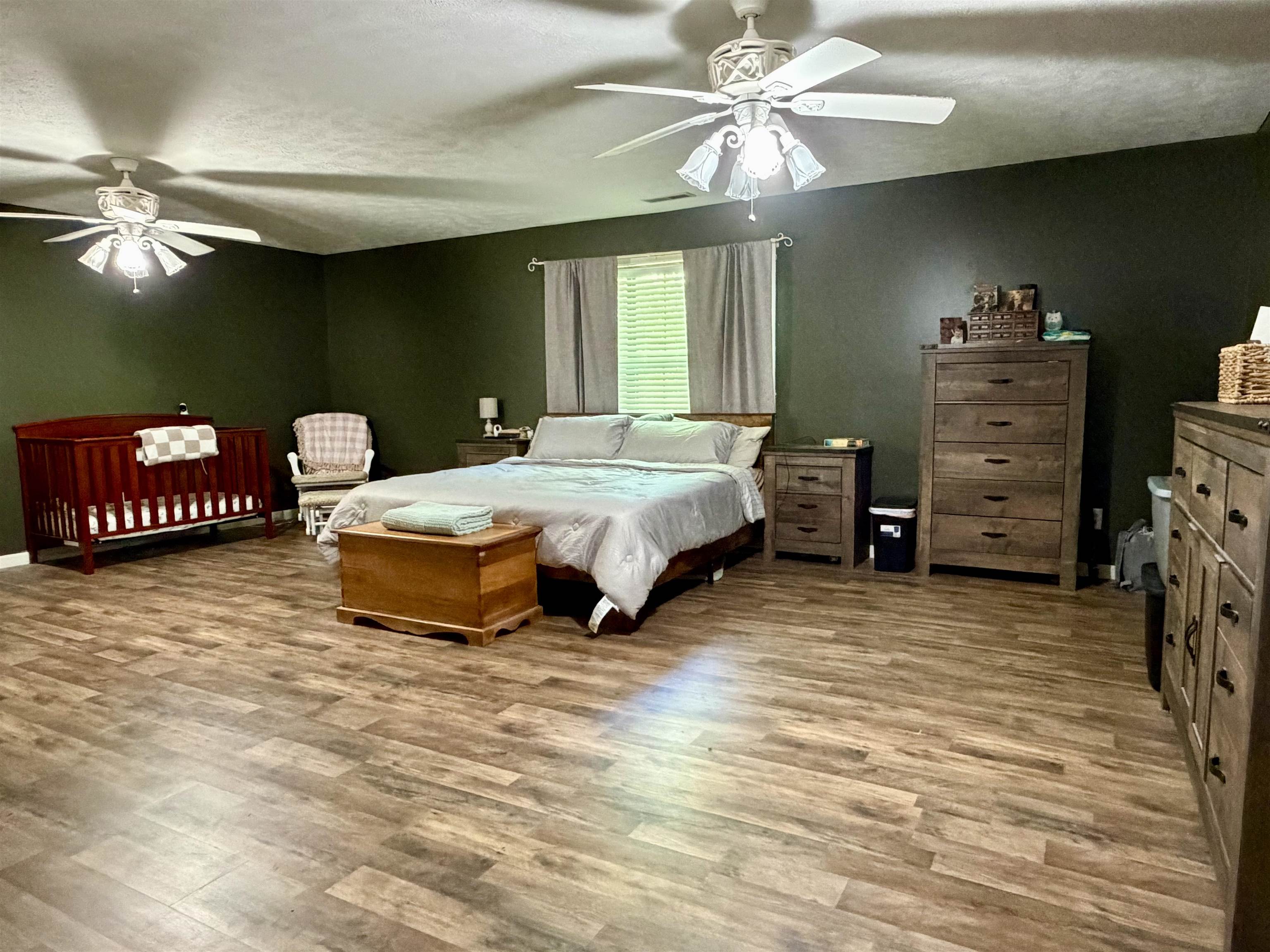 1536 Robinson Shed Road Bethel Springs, TN 38315 - Photo 12 of 23 Spacious room featuring wood-finish flooring, dark green walls, and two ceiling fans with integrated lighting