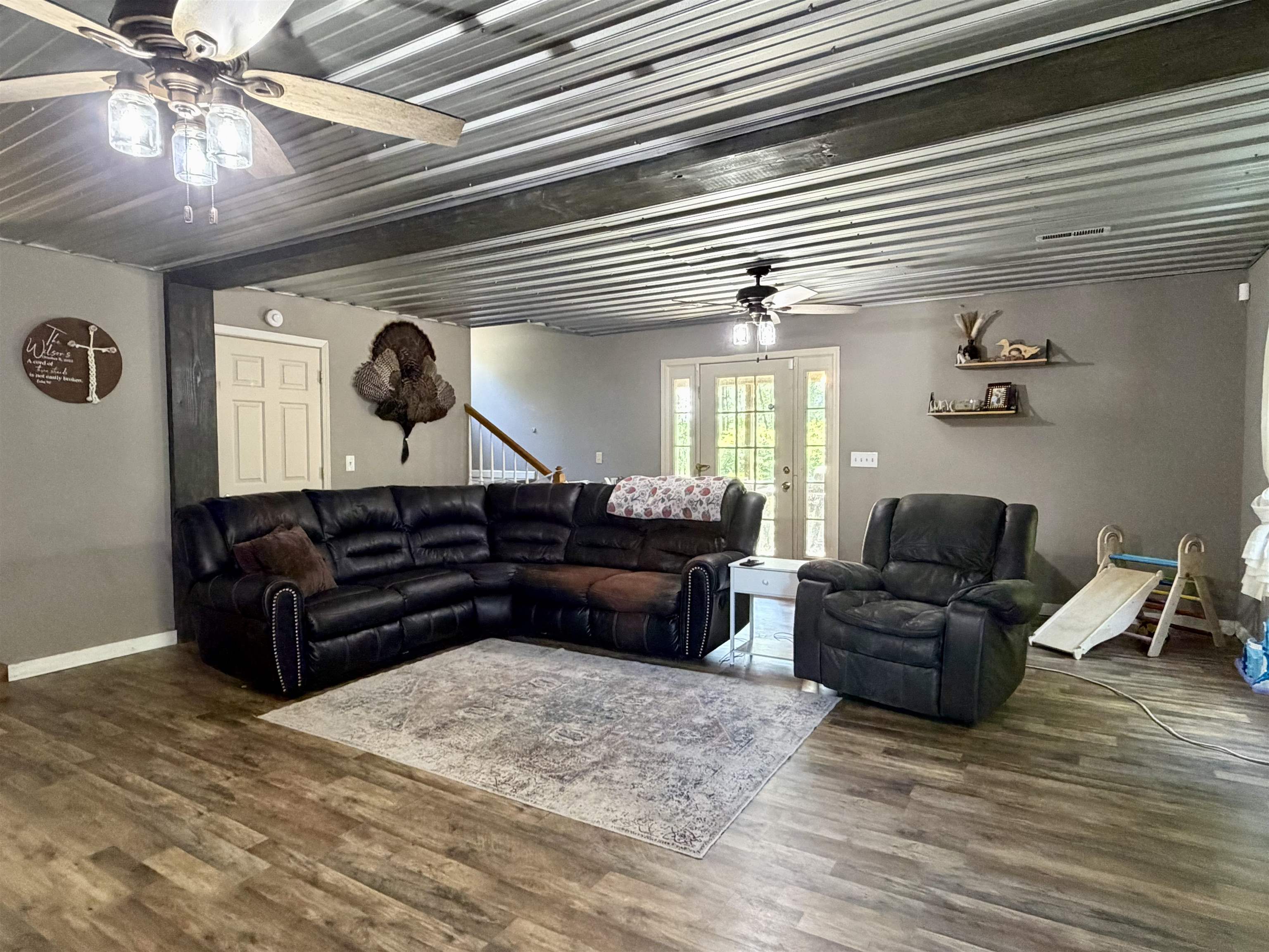 1536 Robinson Shed Road Bethel Springs, TN 38315 - Photo 2 of 23 Spacious living area featuring wood-finish flooring, a corrugated metal ceiling with exposed beams, and ceiling fans with integrated lighting