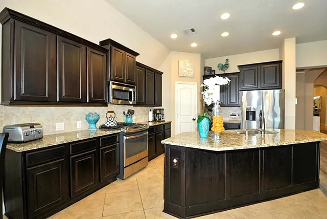 a kitchen with stainless steel appliances granite countertop a sink dishwasher stove top oven and refrigerator with wooden cabinets