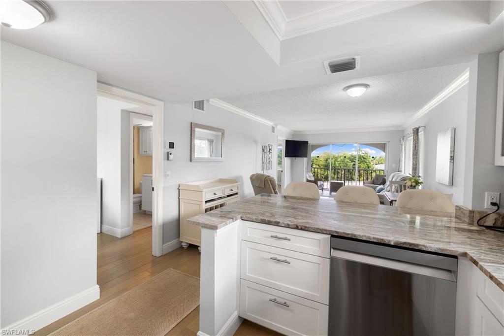 5 High Point Circle West, Unit 307 Naples, FL 34103 - Photo 3 of 31 Kitchen featuring dishwasher, a kitchen breakfast bar, white cabinets, crown molding, and light wood-style floors