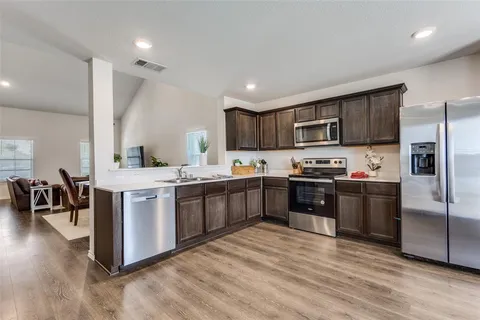 a kitchen with stainless steel appliances kitchen island granite countertop a refrigerator a sink dishwasher a stove with wooden cabinets and floor