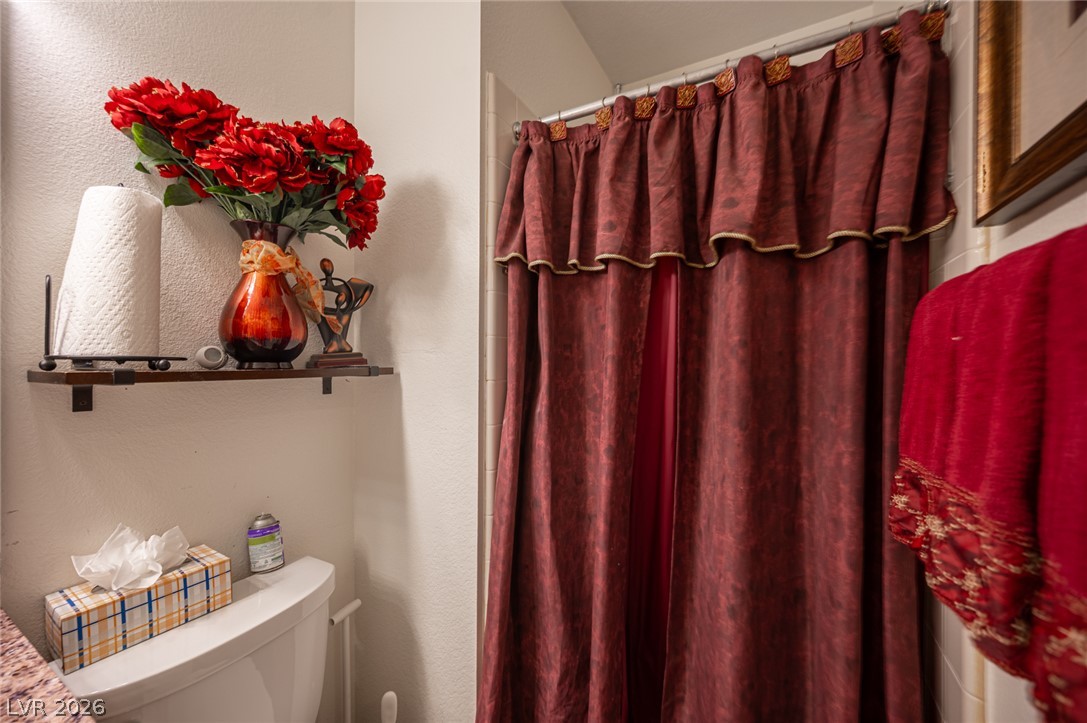 718 Rusty Spur Drive Henderson, NV 89014 - Photo 33 of 50 A well-appointed bathroom features a shower curtain in rich burgundy, complementing the organized wall shelf above the commode.
