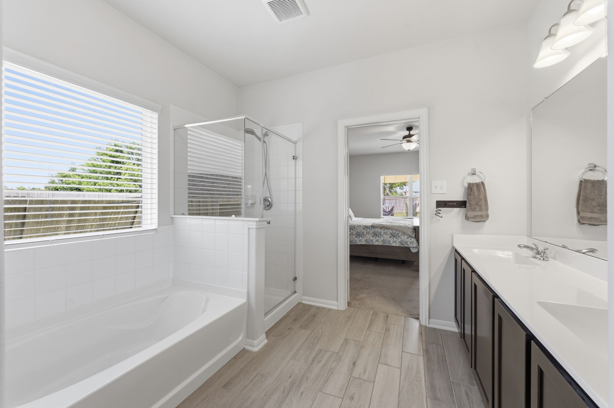 2401 Abbot Brk Drive Rosharon, TX 77583 - Photo 19 of 50 Designed to be both functional and relaxing, this beautifully appointed en-suite bath offers the perfect space to prepare for a busy morning or unwind before an evening out. Features include elegant wood-look tile flooring, dual vanities, soaking tub, and a spacious walk-in shower. A sunny window with blinds brings in natural light while maintaining privacy, and a decorative ceiling fixture adds a touch of sophistication. Completing the retreat are a private water closet and an expansive walk-in closet.