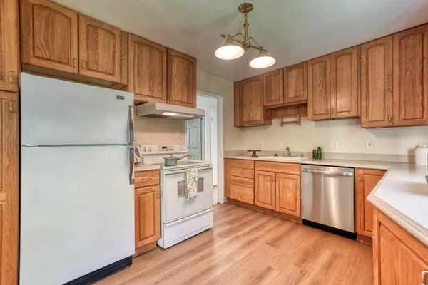 a kitchen with stainless steel appliances granite countertop a refrigerator a stove a sink and white cabinets with wooden floor