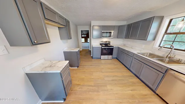 a living room with stainless steel appliances furniture a rug and a kitchen view