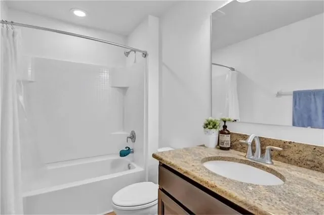 a bathroom with a granite countertop bathtub shower sink vanity mirror and toilet