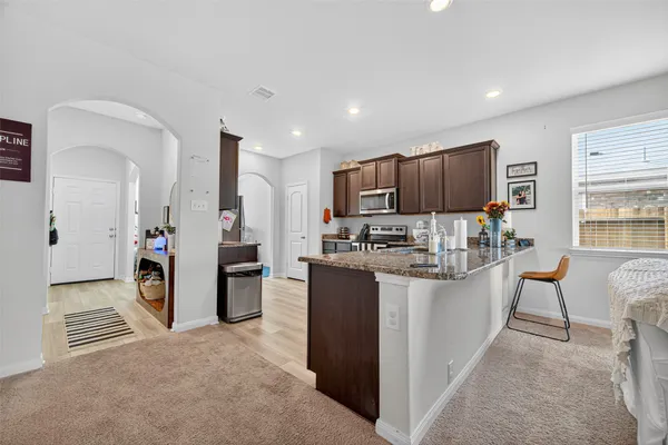 a kitchen with stainless steel appliances kitchen island granite countertop a refrigerator oven a sink dishwasher and white cabinets with wooden floor