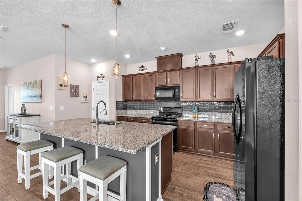 6230 Plover Meadow Street Lithia, FL 33547 - Photo 14 of 50 a kitchen with kitchen island granite countertop a table chairs microwave and refrigerator
