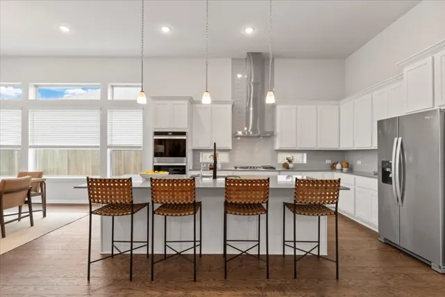a kitchen with stainless steel appliances kitchen island granite countertop a dining table chairs and a refrigerator