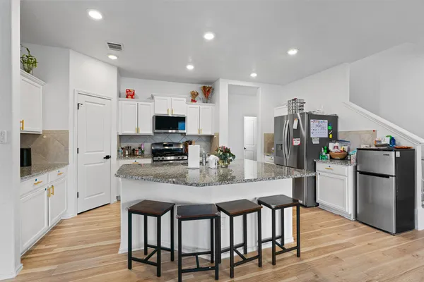 a kitchen with stainless steel appliances kitchen island granite countertop a dining table chairs and refrigerator