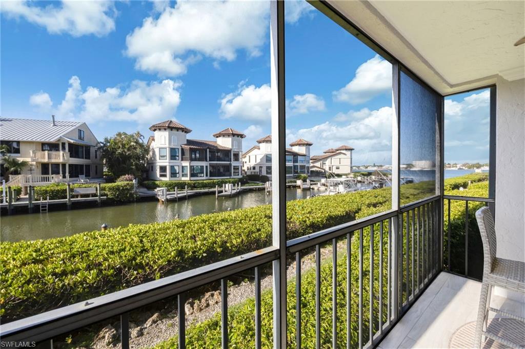1200 Blue Point Avenue, Unit A2 Naples, FL 34102 - Photo 24 of 30 This property features a screened-in balcony with a railing, offering views of a waterway, lush green landscaping, and distant structures