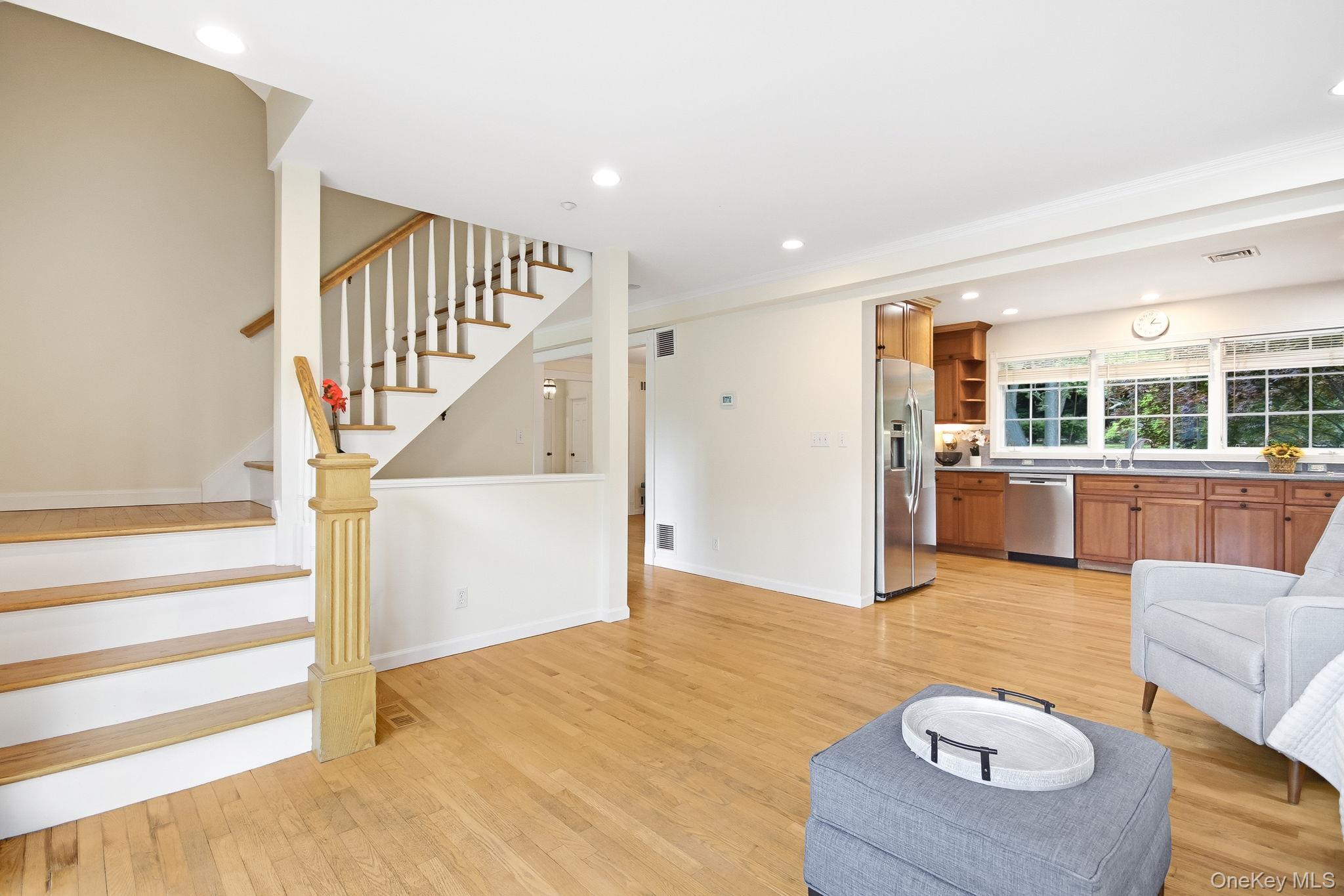 26 Century Ridge Road Purchase, NY 10577 - Photo 13 of 50 Family room alternate view; hardwood flooring spans this room featuring a staircase with white risers and a light wood handrail which leads to 2 upstairs bedrooms; open flow to kitchen and living room