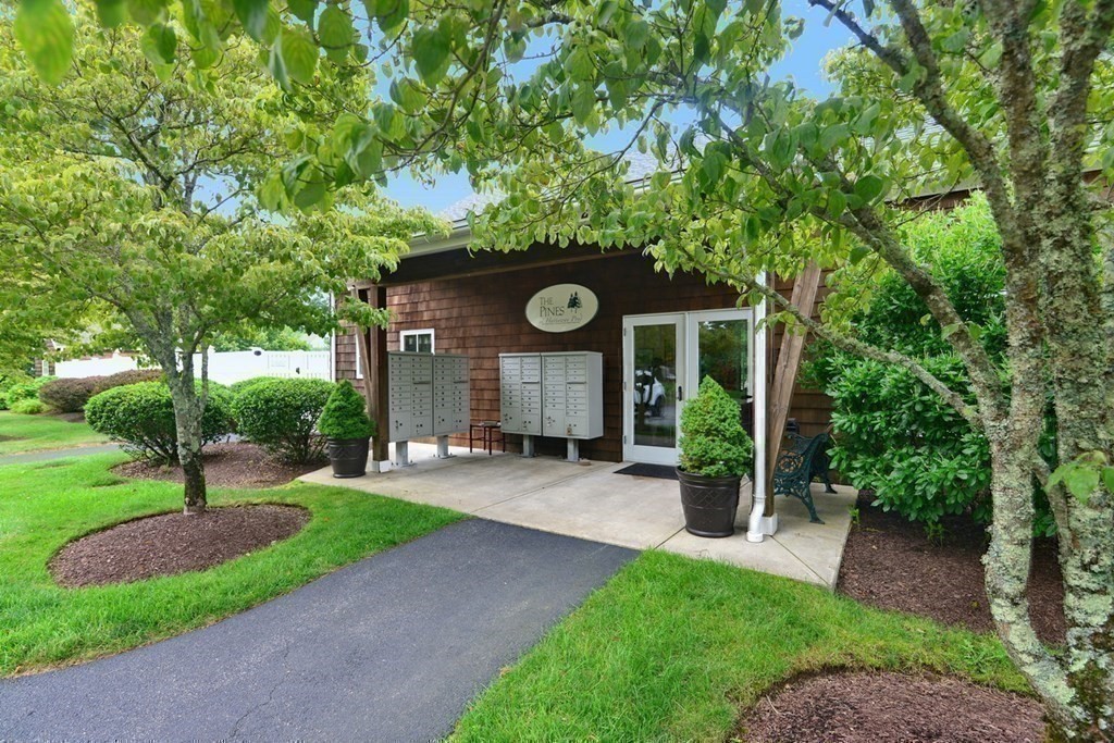 15 Hathaway Pond Circle, Unit 15 Rochester, MA 02770 - Photo 29 of 36 a wooden bench sitting in front of a house with potted plants and large trees
