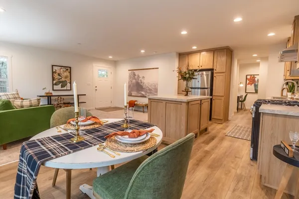 a kitchen with stainless steel appliances granite countertop a stove a sink a refrigerator white cabinets and couches with wooden floor