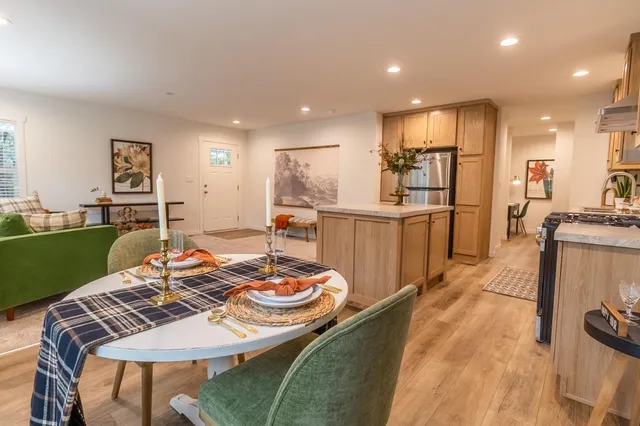 a kitchen with stainless steel appliances granite countertop a stove a sink a refrigerator white cabinets and couches with wooden floor