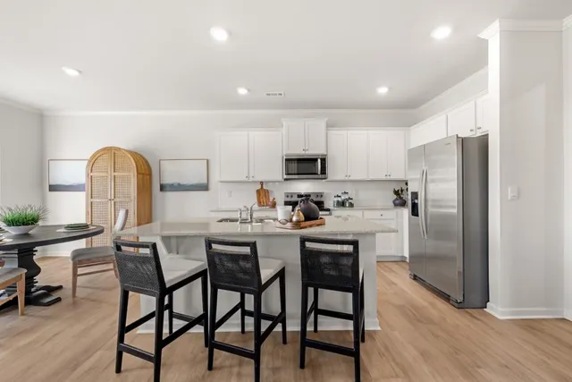 a kitchen with stainless steel appliances granite countertop a dining table chairs refrigerator and sink