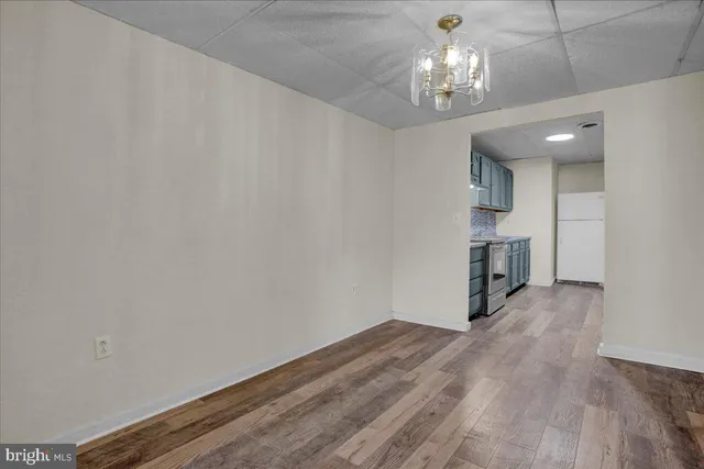 a view of empty room with wooden floor and kitchen