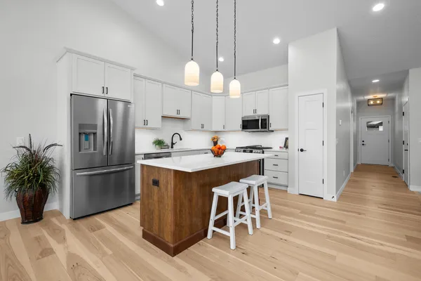 a kitchen with stainless steel appliances a refrigerator a stove a sink dishwasher and a dining table with wooden floor