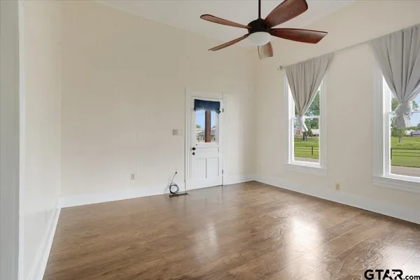an empty room with wooden floor chandelier fan and windows