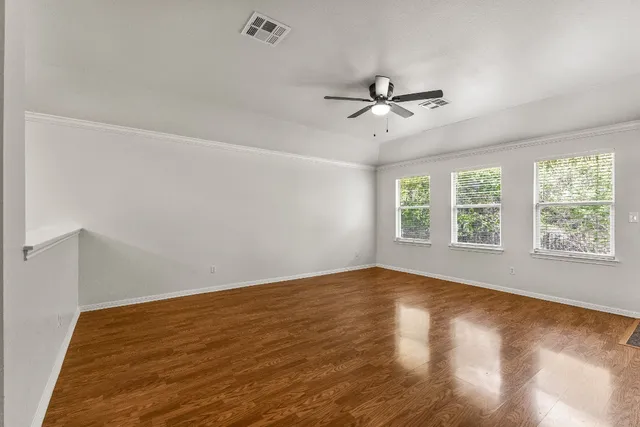 an empty room with wooden floor fan and windows