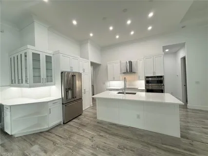 a view of an empty room with wooden floor and a kitchen