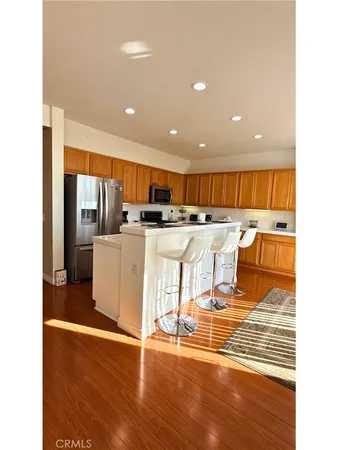 a kitchen with stainless steel appliances kitchen island granite countertop a stove top oven a sink a refrigerator and white cabinets with wooden floor