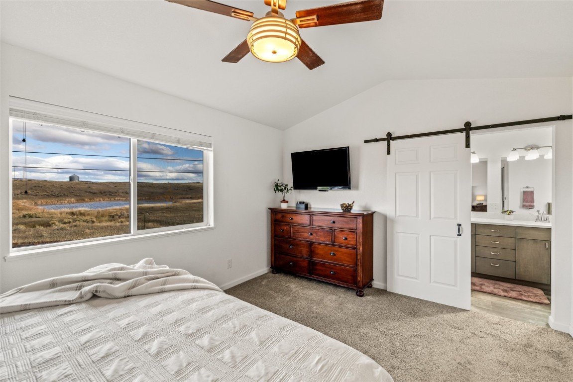 307 Little Bend Road Hayden, CO 81639 - Photo 29 of 41 Bedroom with a barn door, light carpet, vaulted ceiling, connected bathroom, and ceiling fan