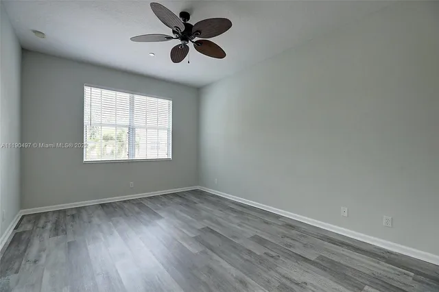 an empty room with wooden floor ceiling fan and windows