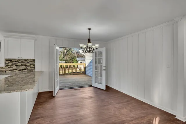 an empty room with wooden floor chandelier and windows