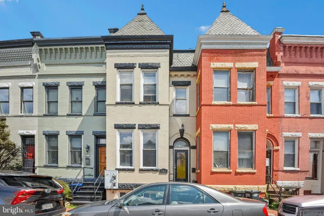 a front view of a building with lot of cars and trees