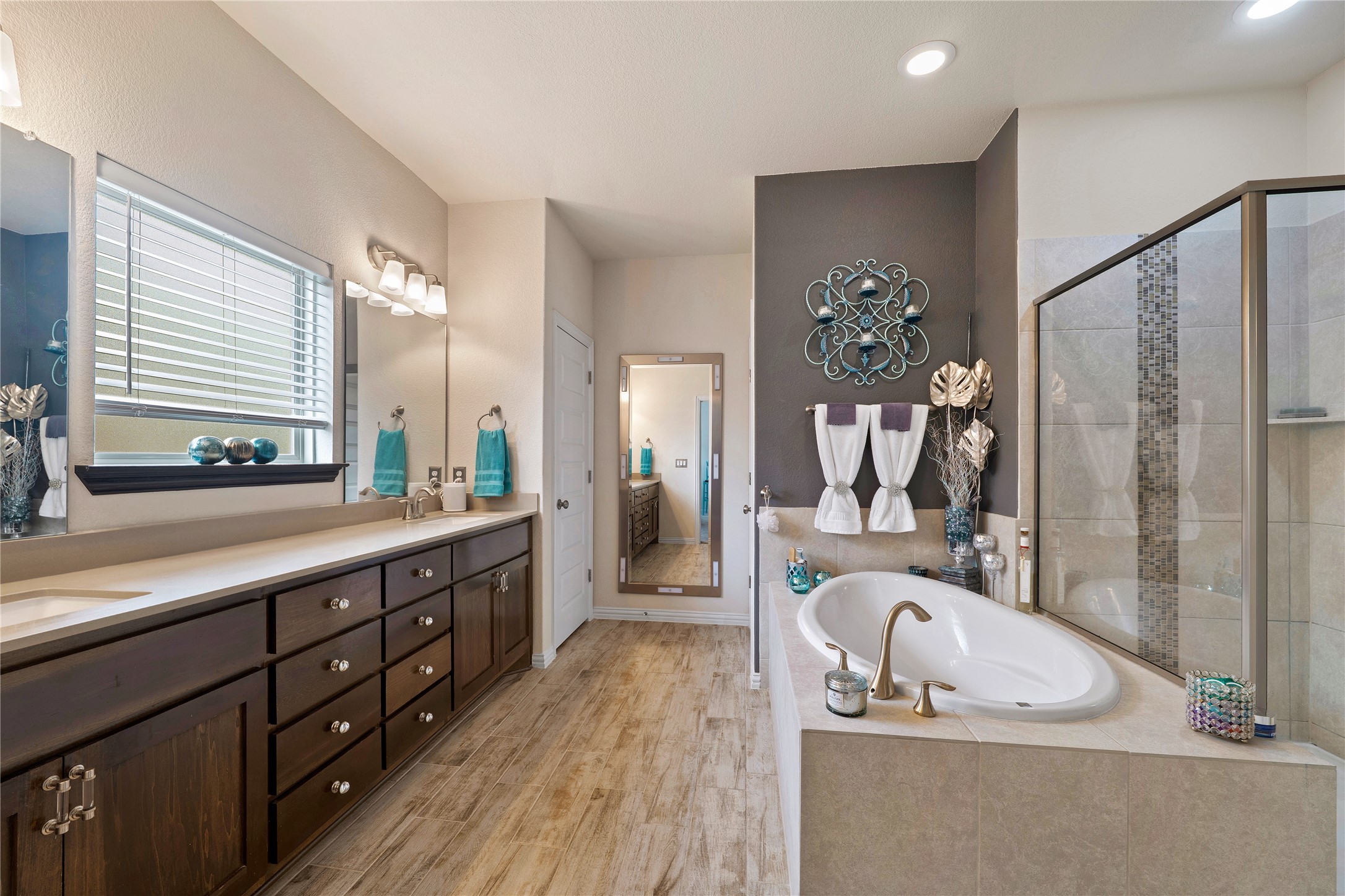 8721 Sikes Way Austin, TX 78747 - Photo 17 of 33 Primary bathroom featuring an oval soaking tub, an enclosed glass shower with tile accents, dual sinks, extensive dark wood cabinetry, and wood-finish flooring