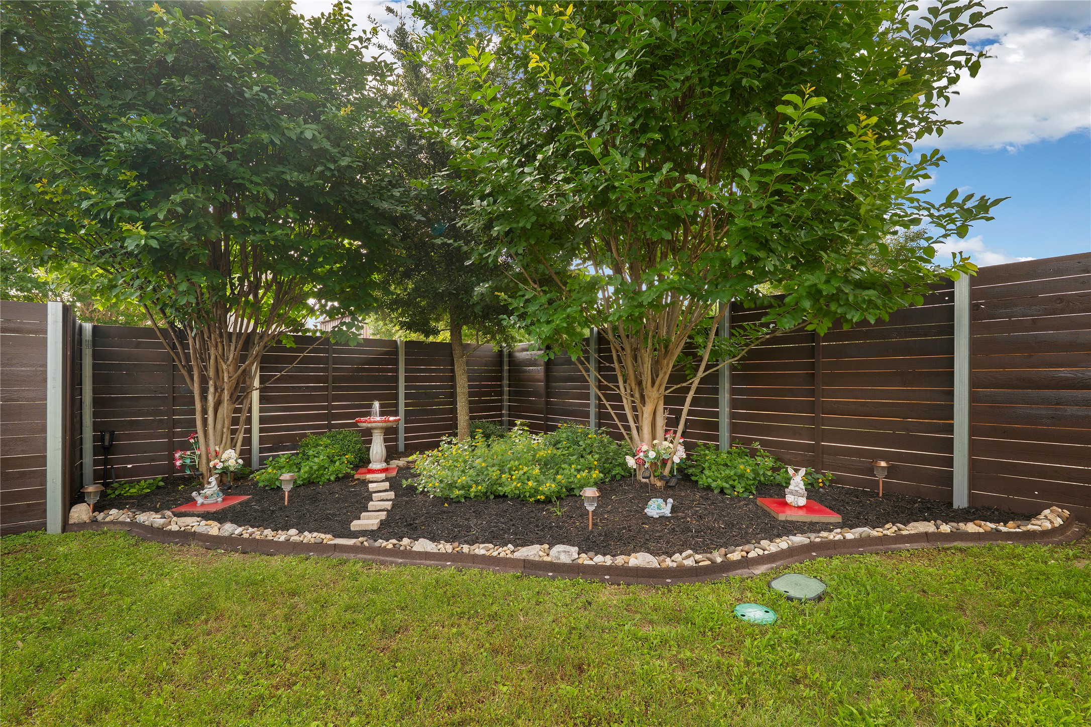 8721 Sikes Way Austin, TX 78747 - Photo 25 of 33 View of landscaped garden bed featuring mature trees, dark mulch, and a decorative bird bath