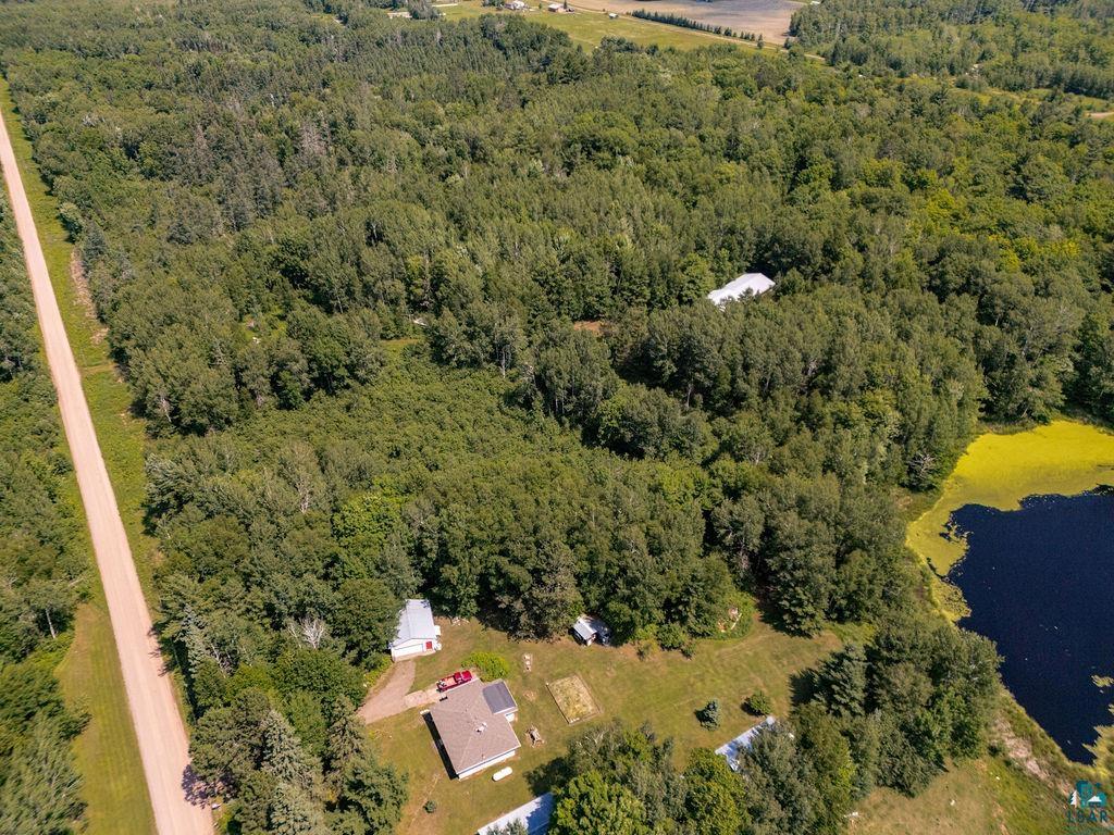 2592 Strandberg Road Barnum, MN 55707 - Photo 36 of 44 Expansive wooded property featuring a natural pond with green vegetation, a gravel road bordering the property, and two distinct structures