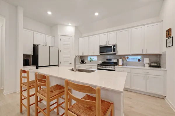 a kitchen with stainless steel appliances granite countertop a stove a sink a microwave a refrigerator and white cabinets with wooden floor