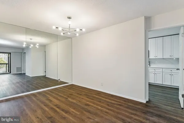 a view of an empty room with wooden floor and a kitchen