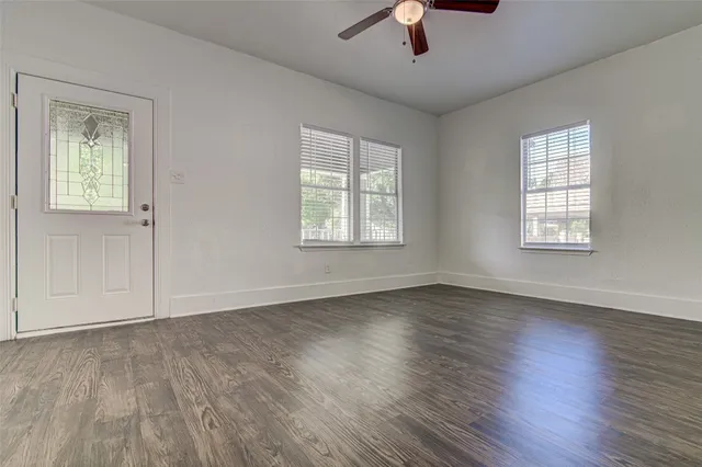 an empty room with wooden floor chandelier fan and windows