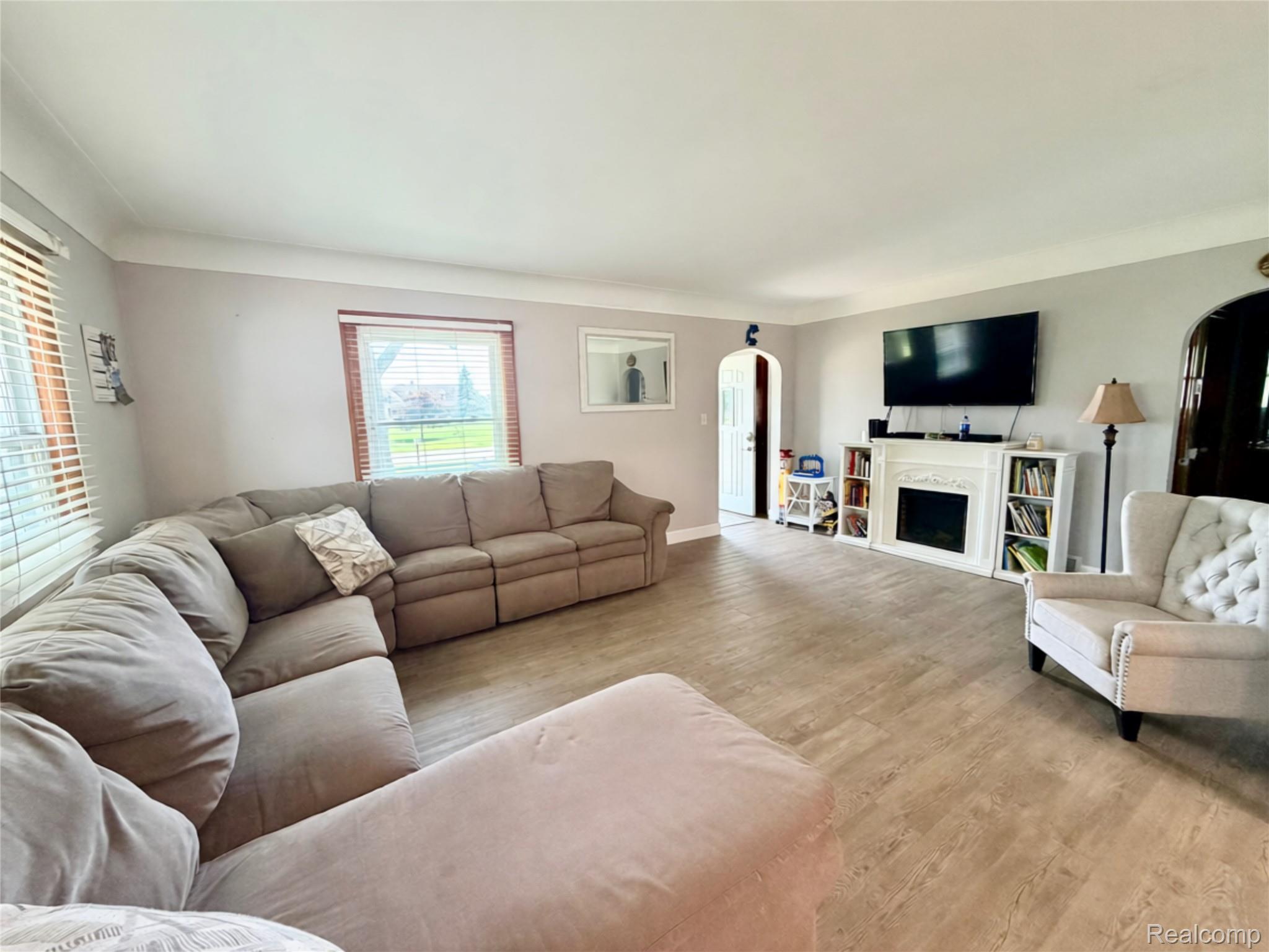 3840 East Dunbar Road Monroe, MI 48161 - Photo 15 of 38 Spacious living area featuring wood-finish flooring, a white mantel with built-in shelving, multiple windows with blinds, and a distinctive arched doorway