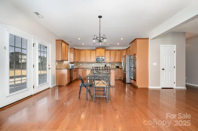 a kitchen with stainless steel appliances a dining table chairs a refrigerator and cabinets