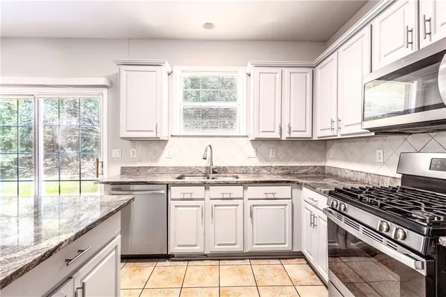 a white kitchen with granite countertop a stove top oven microwave and cabinets