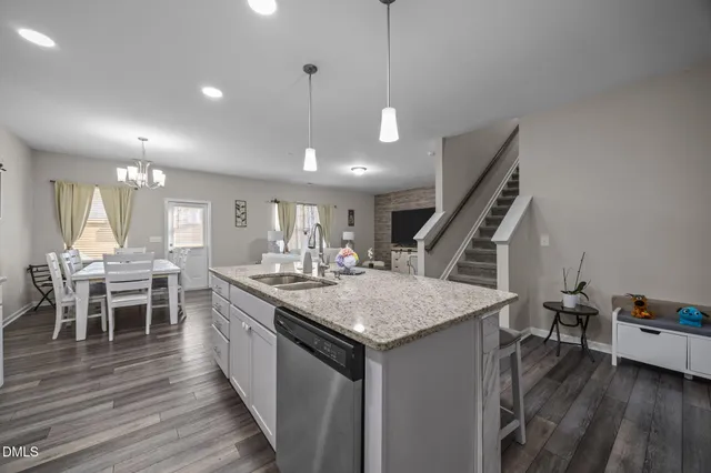 a open kitchen with stainless steel appliances granite countertop a refrigerator a sink dishwasher a oven and a dining table with wooden floor