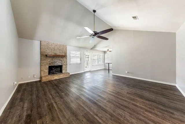 an empty room with wooden floor a ceiling fan a fireplace and windows