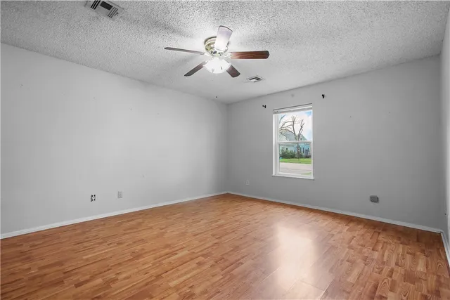 an empty room with wooden floor ceiling fan and windows