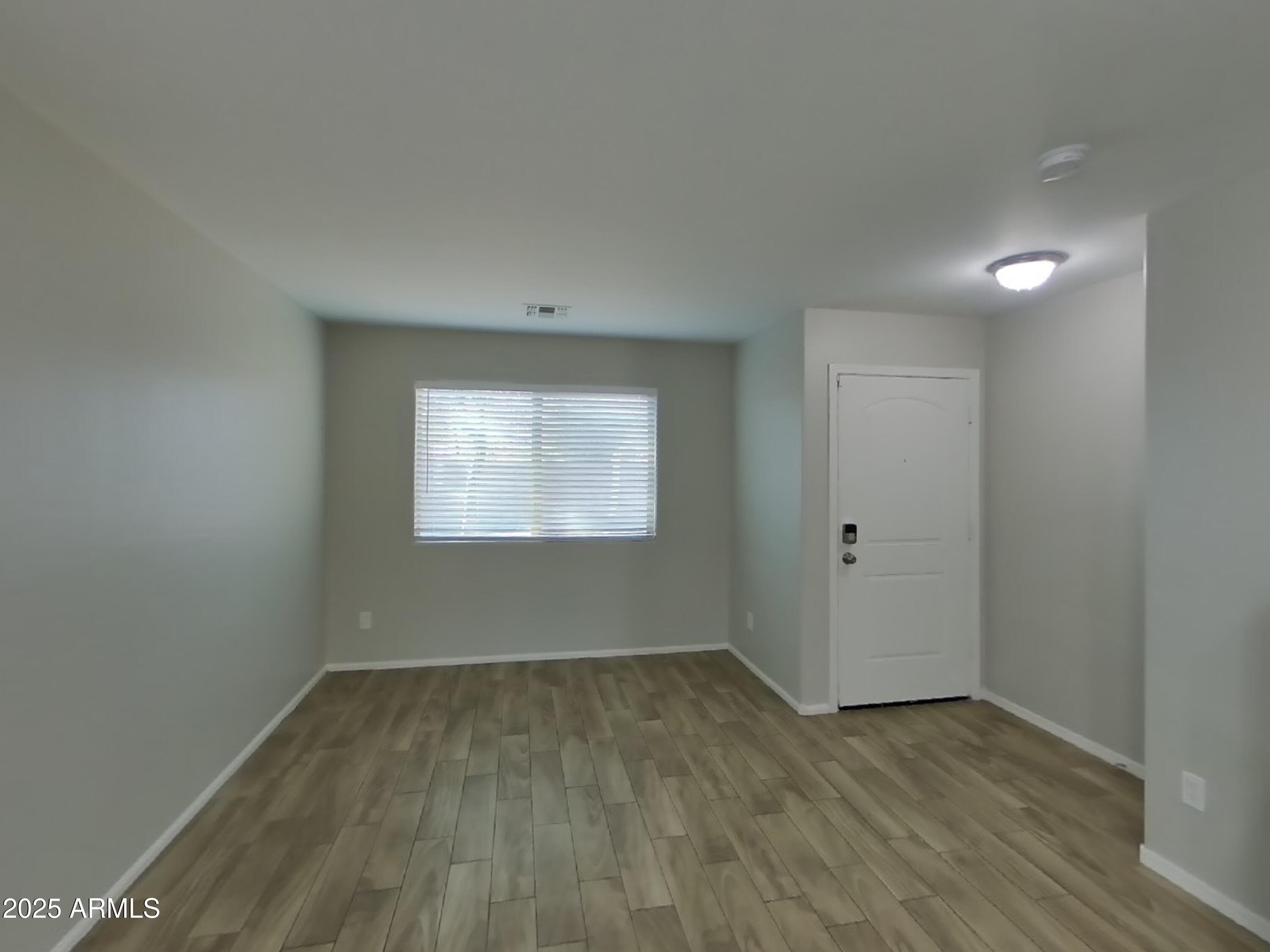 3513 South 89th Avenue Tolleson, AZ 85353 - Photo 2 of 19 a view of an empty room with wooden floor and a window