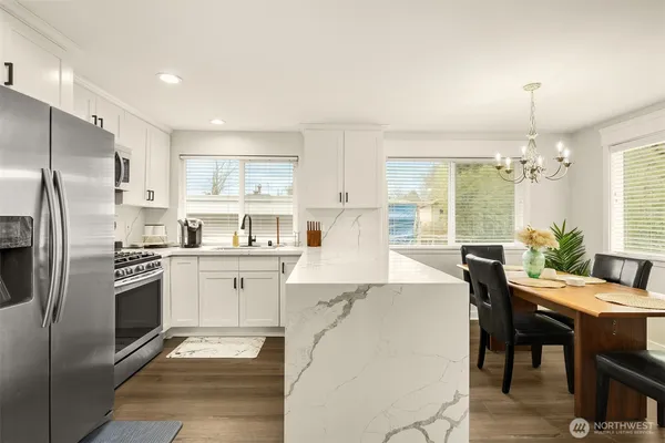 a kitchen with stainless steel appliances kitchen island granite countertop a refrigerator a stove a sink dishwasher and white cabinets with wooden floor