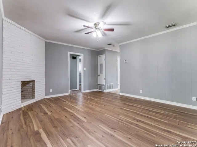 a view of an empty room with wooden floor fireplace and a window