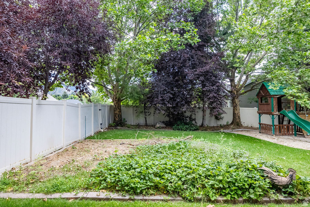 288 525 South Providence, UT 84332 - Photo 66 of 71 Expansive backyard featuring a white vinyl privacy fence, mature trees, a wooden play structure with a green slide, and varied ground cover
